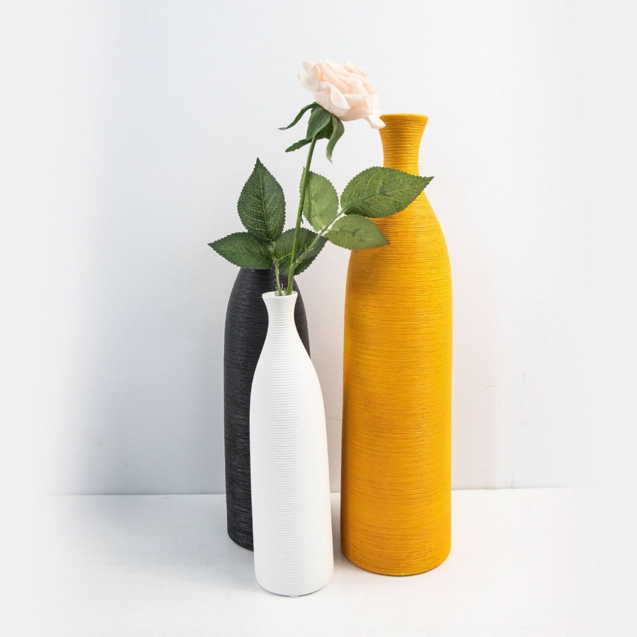 Three minimalist ceramic vases (white, black, yellow) with textured finish, one holding a rose.